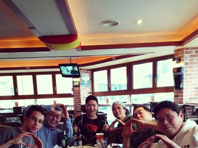 There are few people sat around the table. The table has many food items and beer glass. It seems...