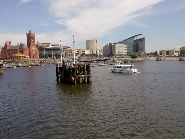 In this image we can see castle, buildings, boat, water, sand and trees.